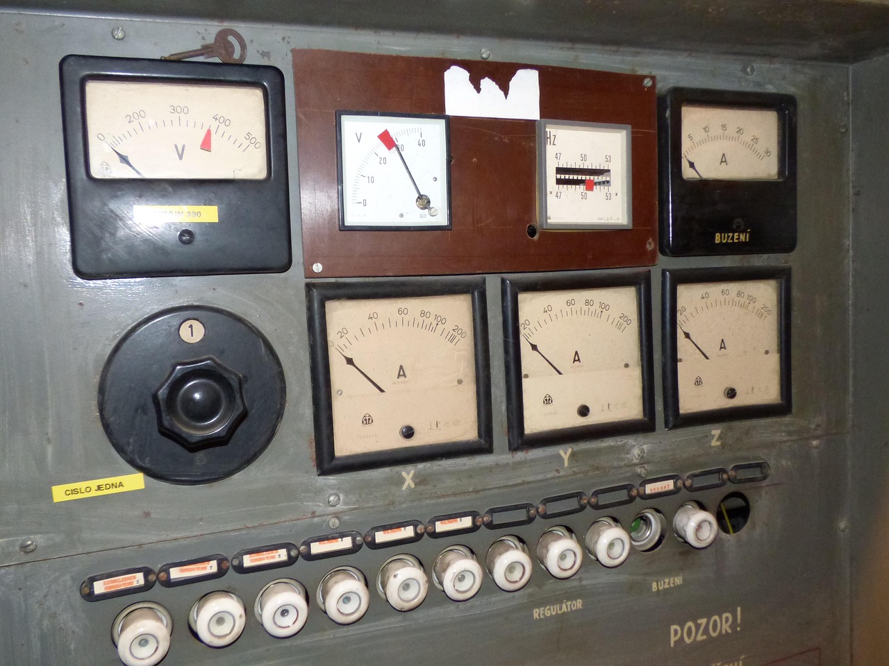 Bank of analog voltage and current meters above ceramic fuse holders on an old panel